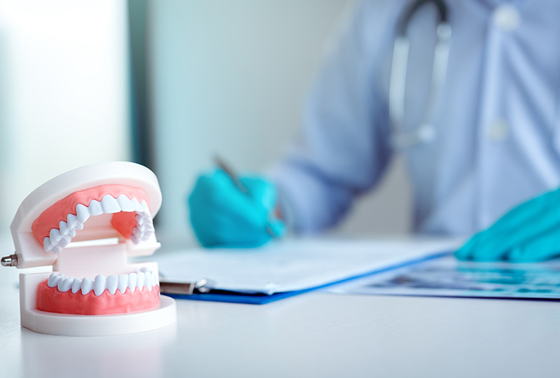 A dental professional wearing gloves and a stethoscope, sitting at a desk with a dental model and document.